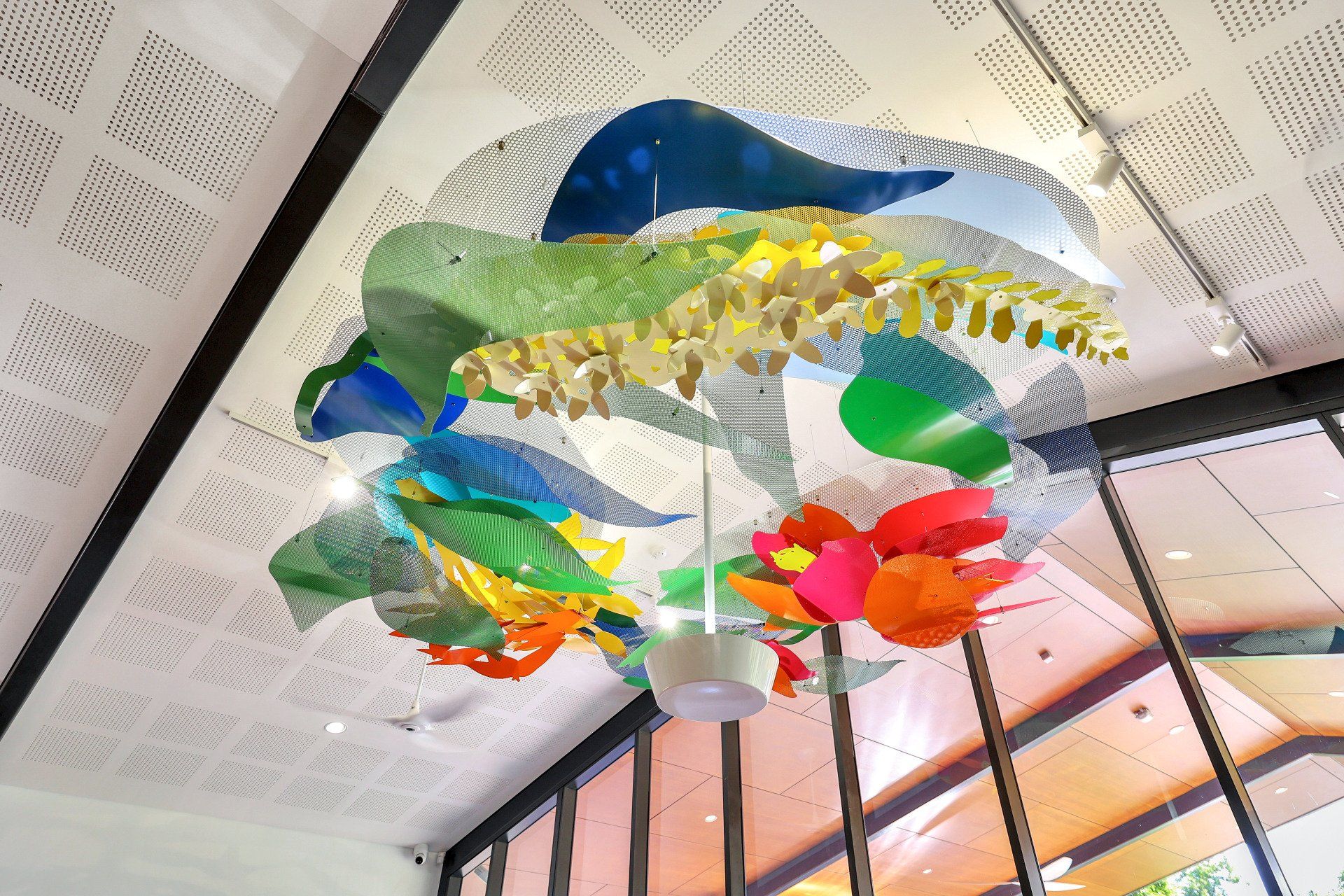Colorful, layered, circular art installation suspended from a white ceiling with angled cutouts, viewed from below.