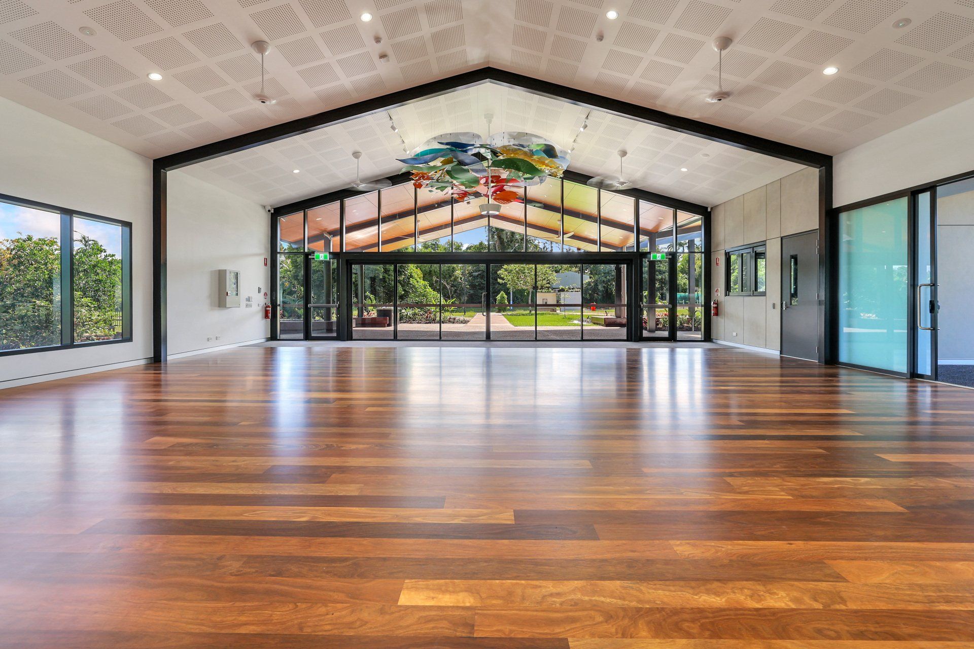 Brand new community hall with wooden floors facing out to a floor to ceiling window of green garden