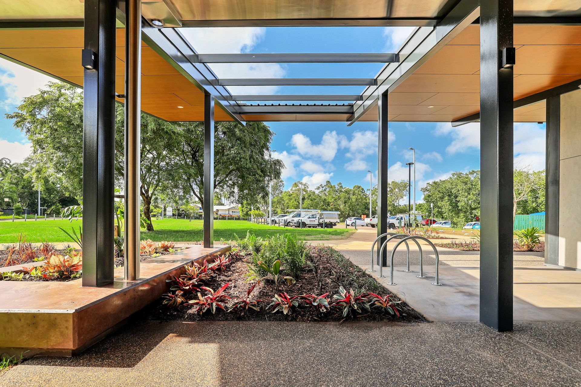 Covered walkway with garden, grassy park, and blue sky visible through the opening.