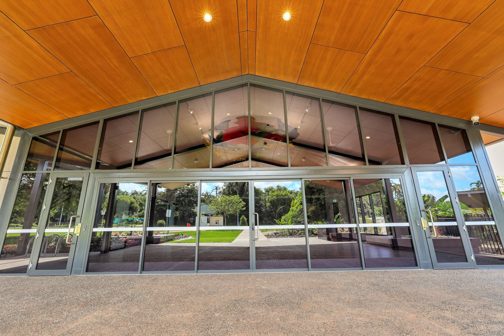 Glass sliding doors lead into a building with a wood-paneled ceiling, reflecting an outdoor landscape.