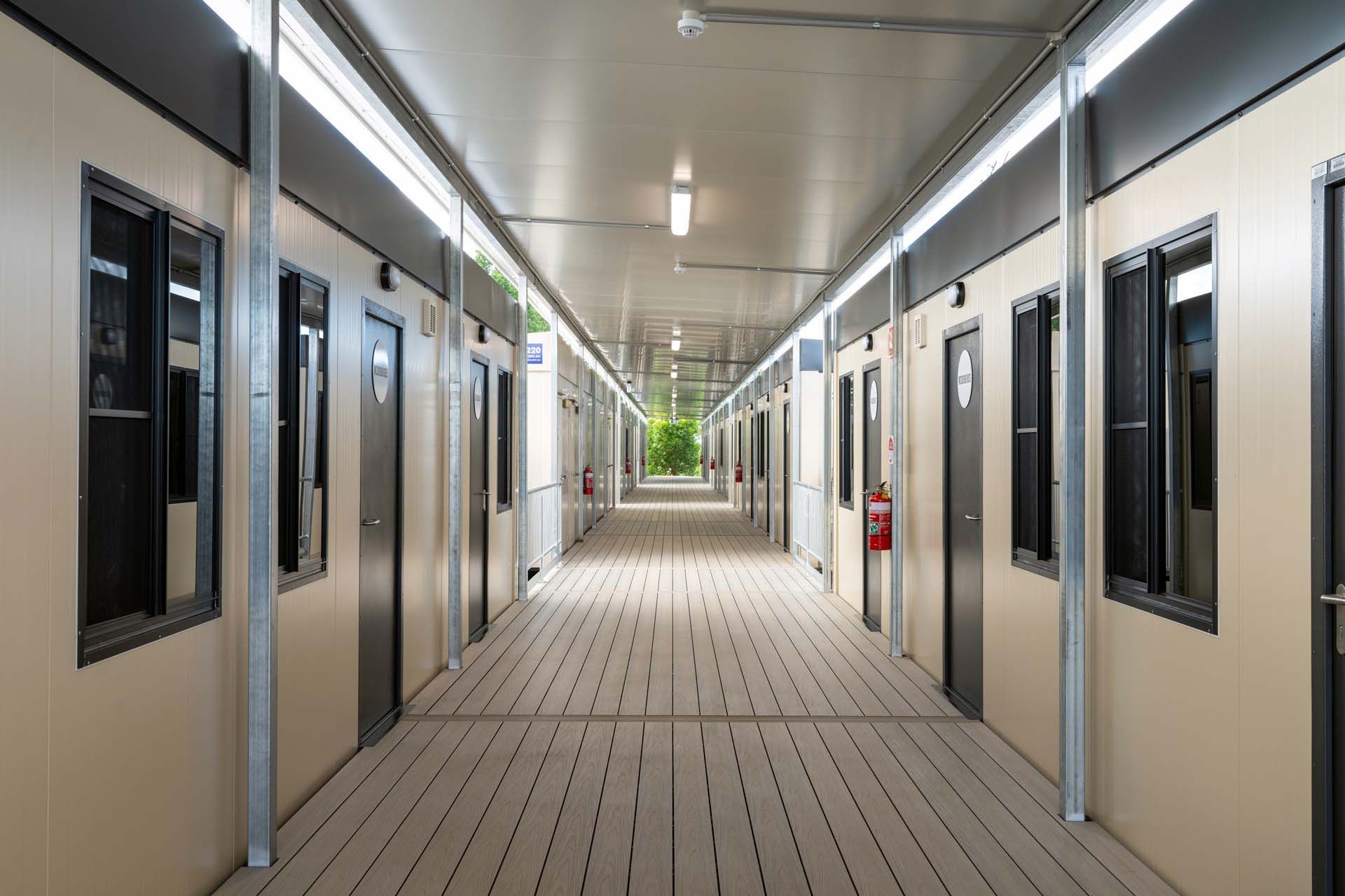 Long hallway with doors on either side separating two buildings with a tree in the distance