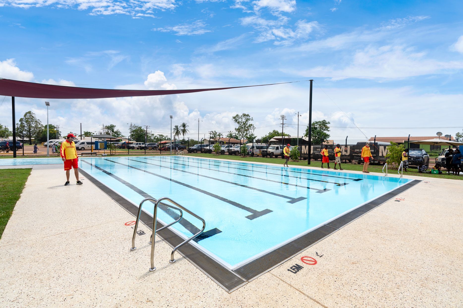 An outdoor swimming pool with a lifeguard on duty under a blue sky.