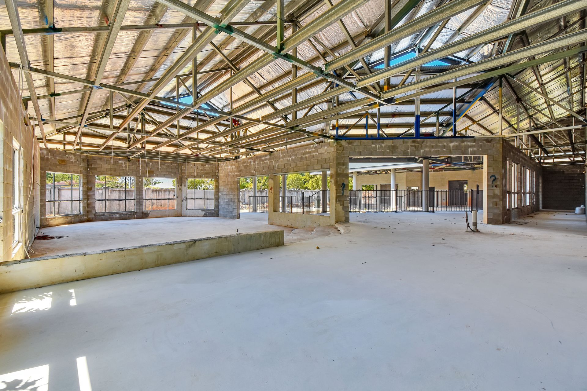 Interior view of a building under construction; concrete floor, open-frame roof, columns, and windows.