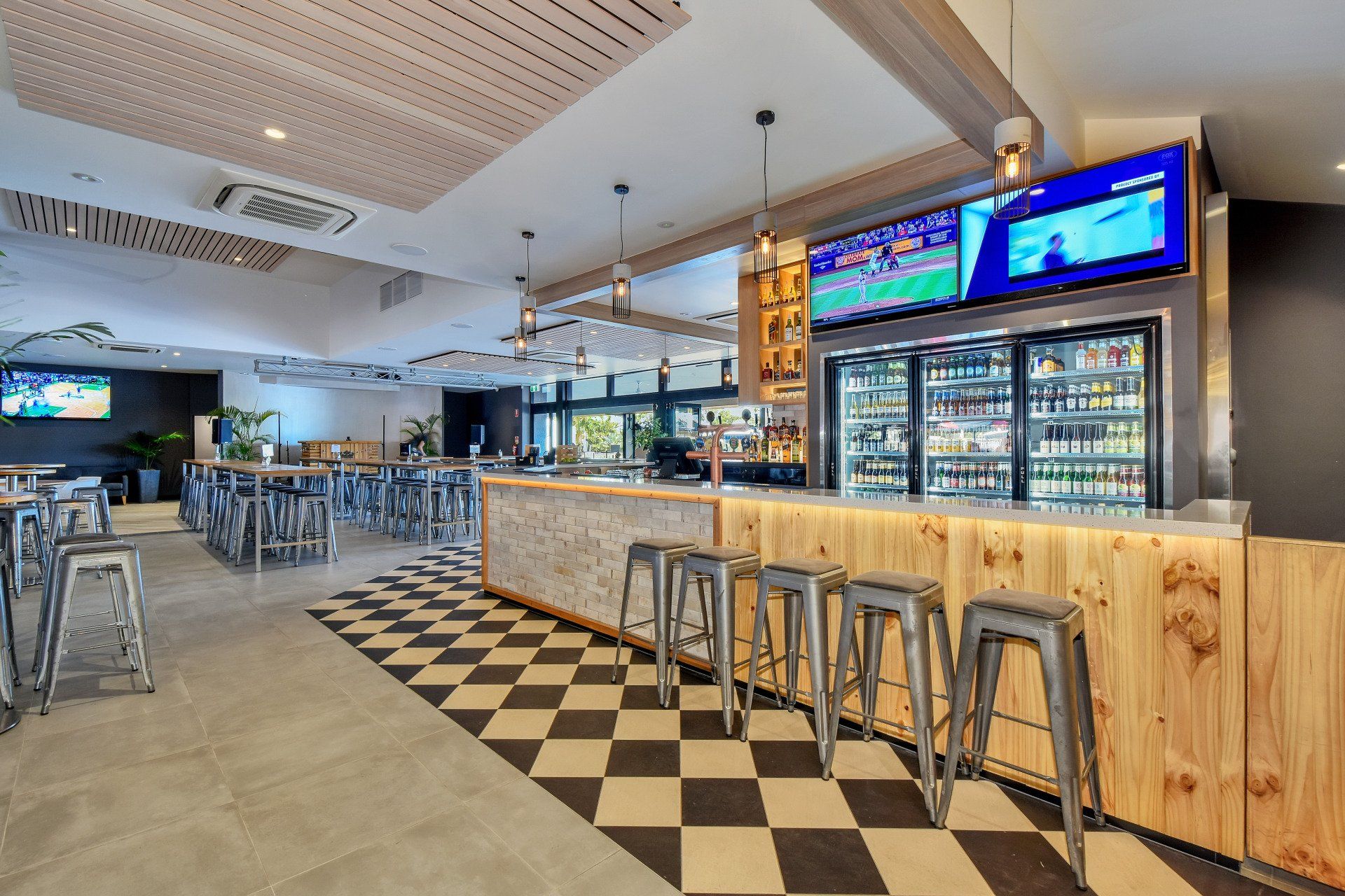 Bar interior with stools, drinks, TV screens, and checkered floor.