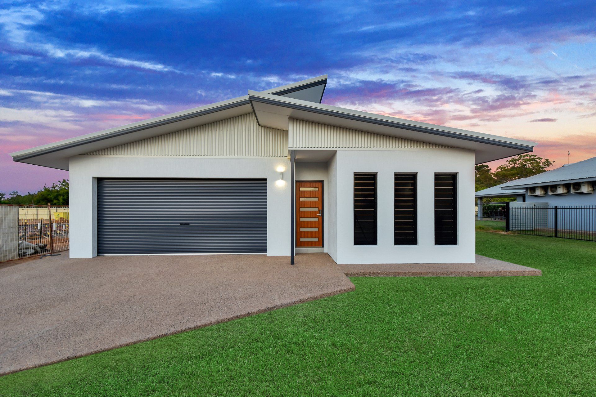 White house with gray garage door, brown front door, and green lawn against a colorful sunset.
