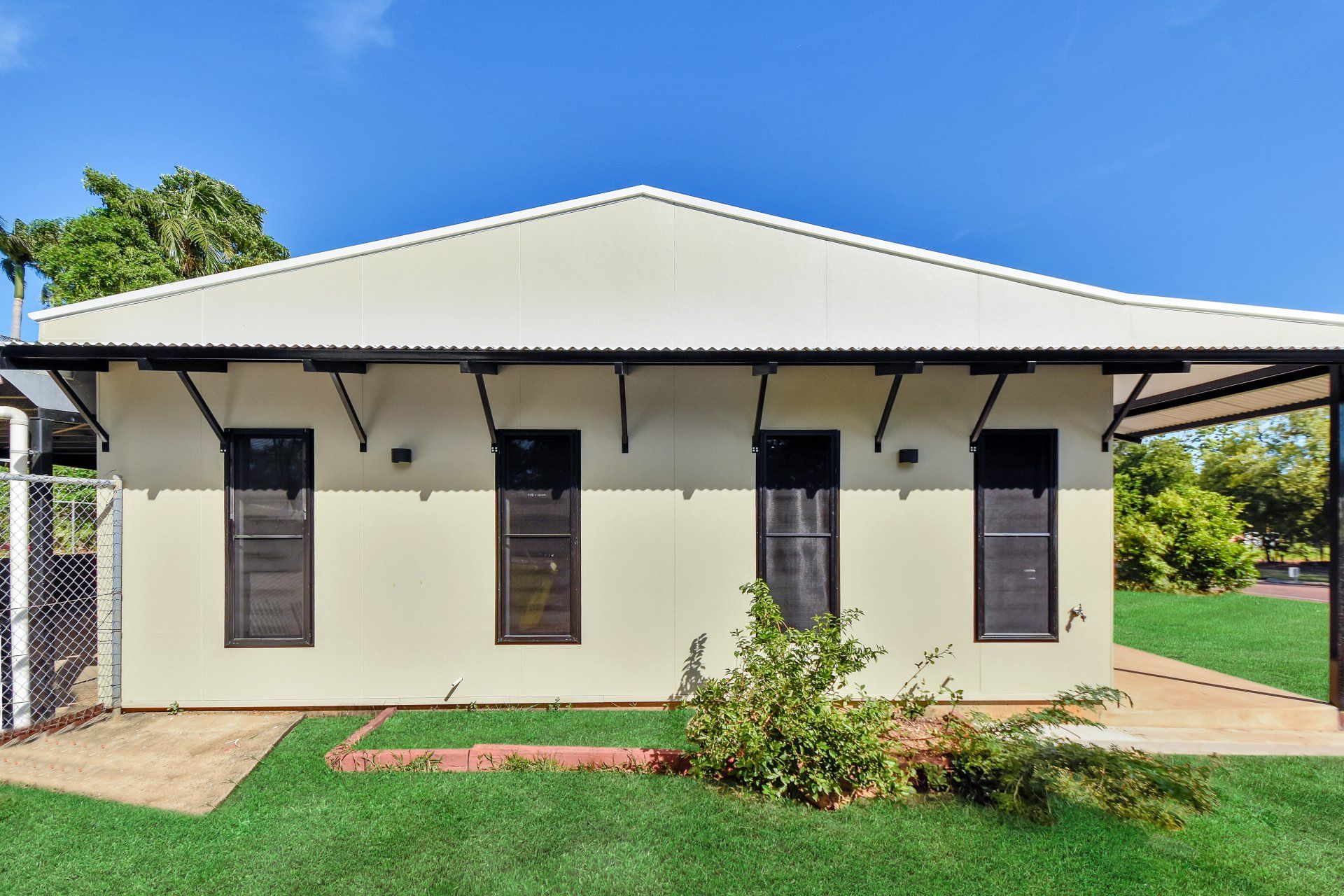 Beige bungalow with a metal roof, louvre windows, and a small awning. Green lawn.