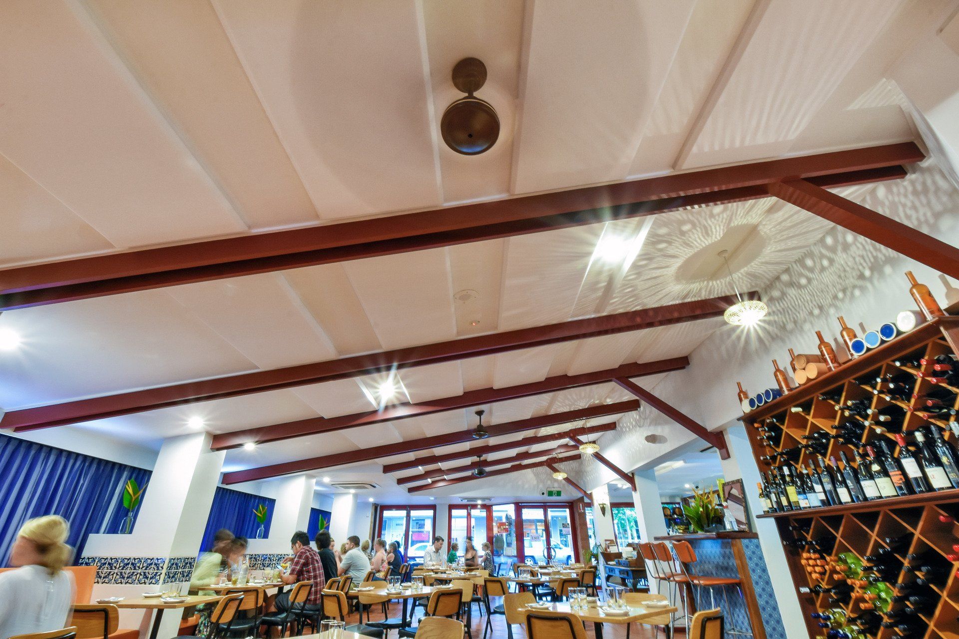 Restaurant interior with tables, diners, and a ceiling fan. Wine bottles are visible.