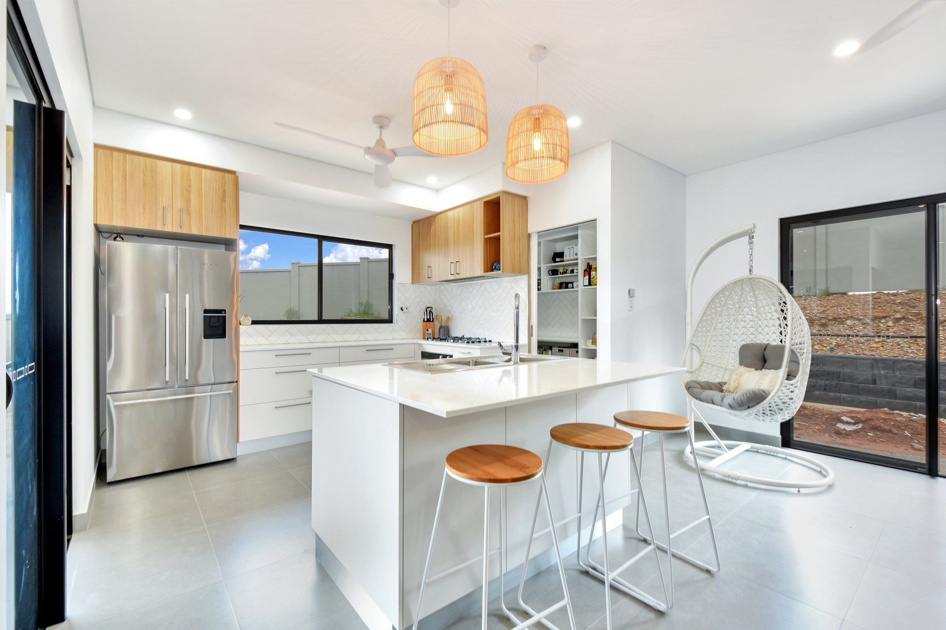 Open plan kitchen with breakfast bench and hanging egg chair nearby.