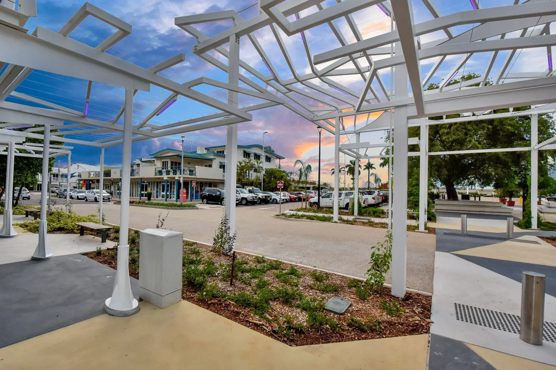White trellis structure overlooking a street with parked cars and buildings. Blue and pink sky.