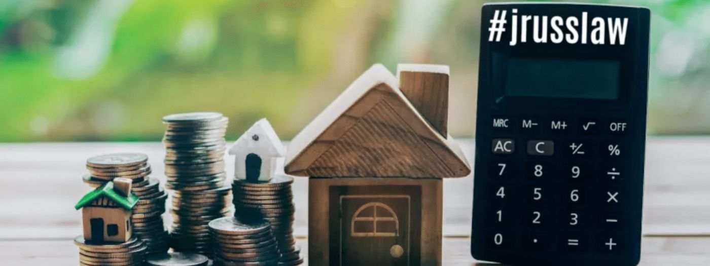 A calculator is sitting on a wooden table next to a model house and stacks of coins.