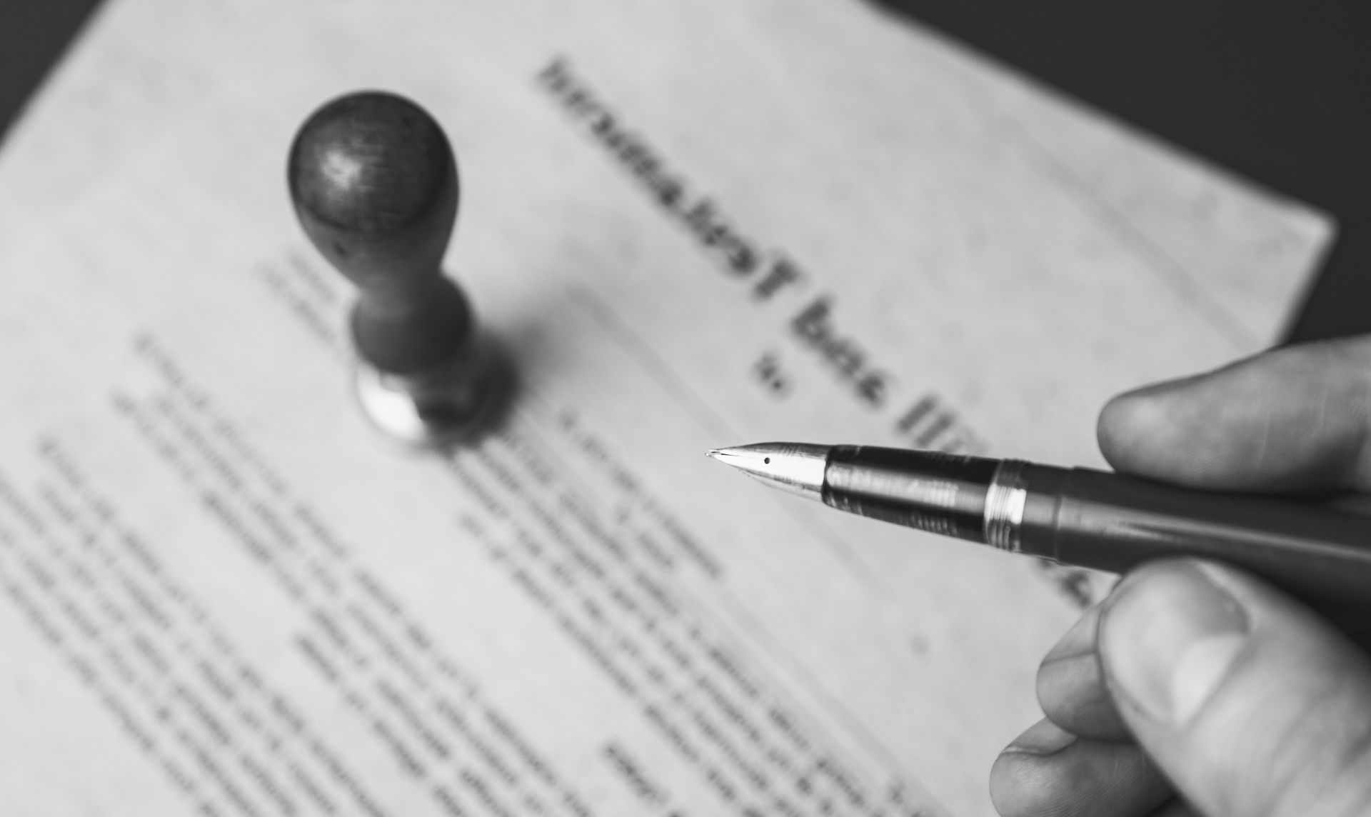 A person is signing a document with a pen and a stamp.