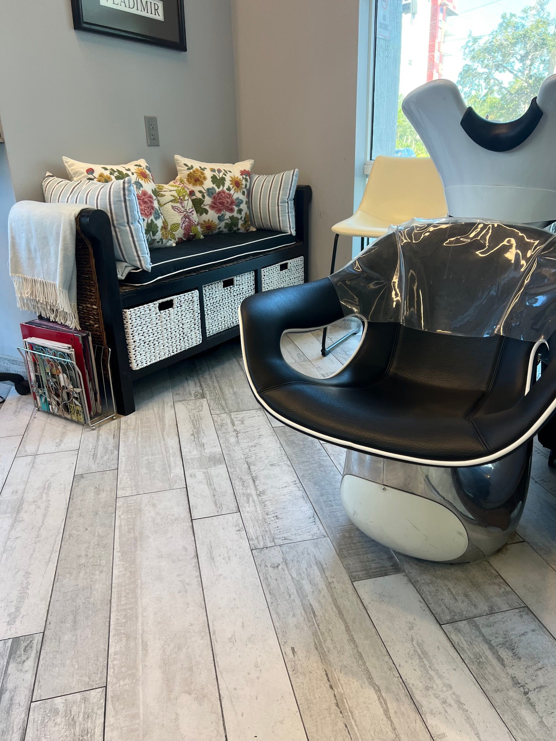 Black chair and bench with floral pillows, baskets, and a blanket in a room with a window.