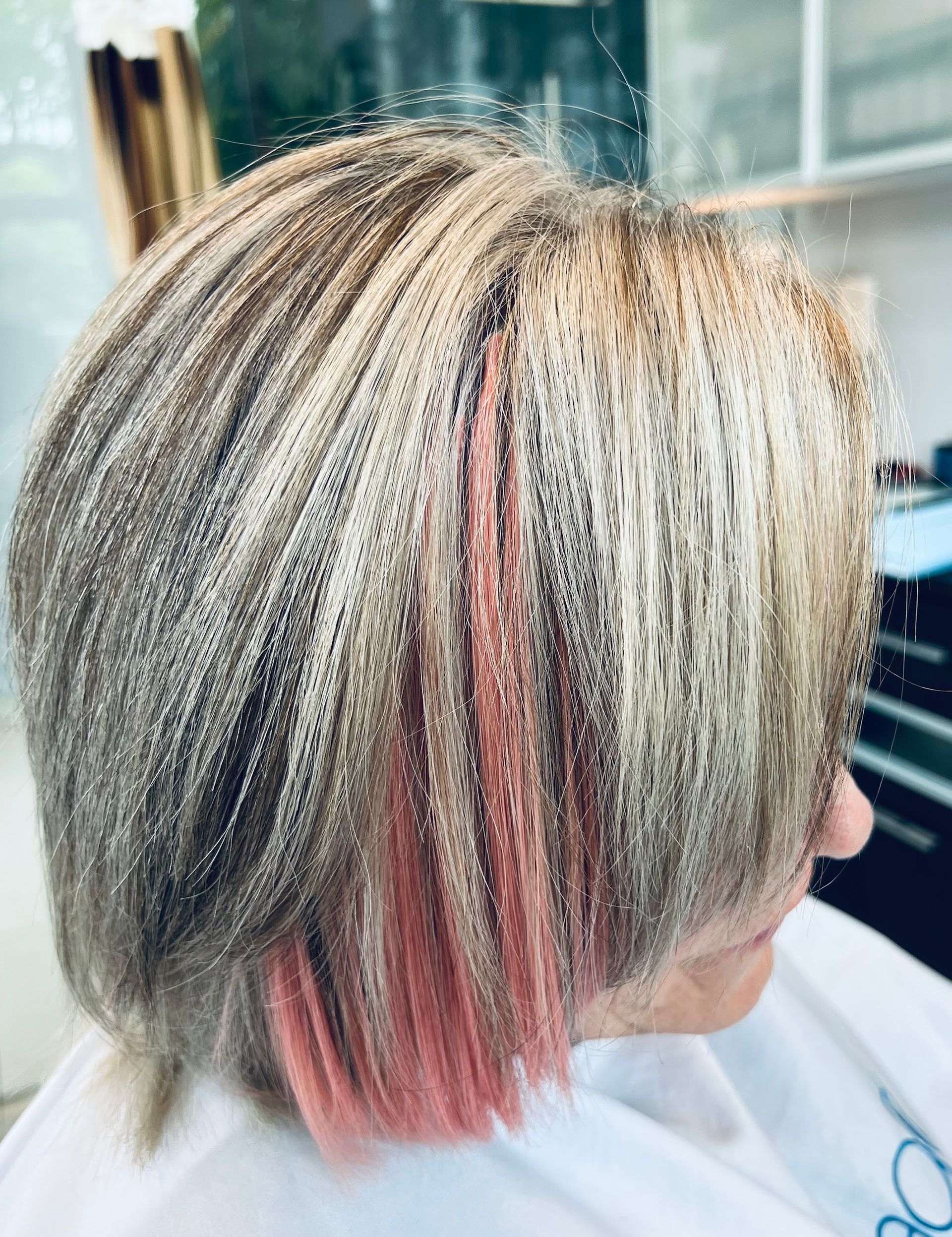 Person with short, textured, gray-blonde hair with pink highlights, in a salon setting.