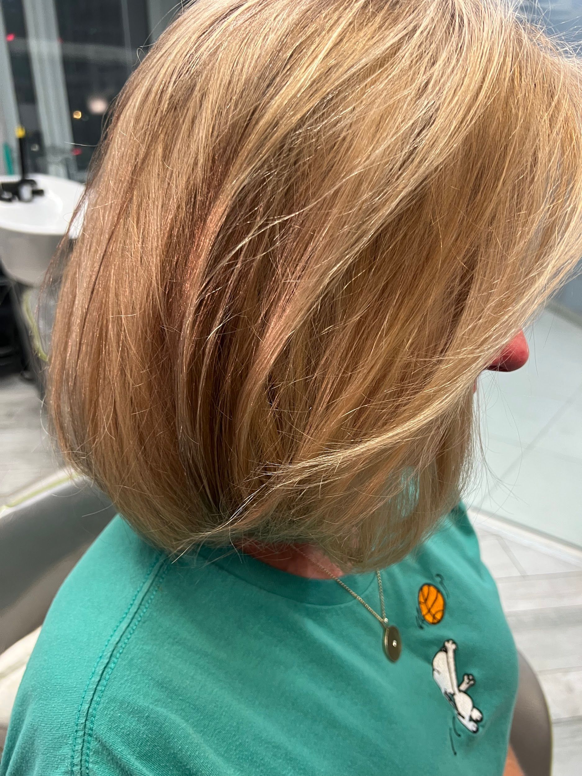 Person with blonde hair covered in glitter, wearing a green shirt, in a salon.
