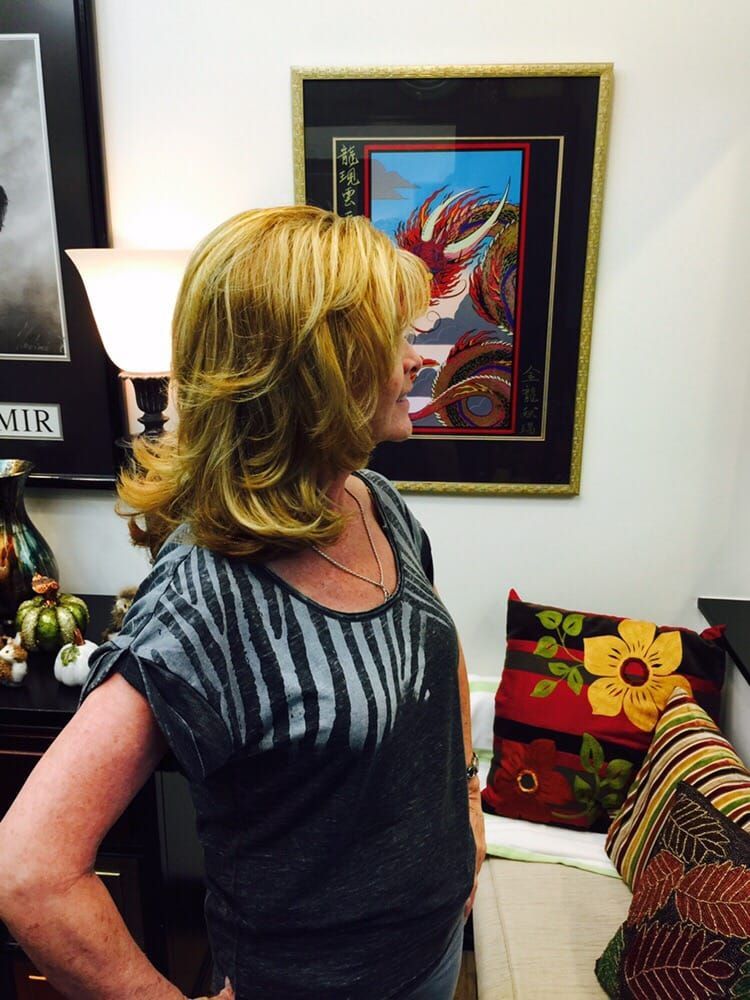 Woman with layered blonde hair, in front of a wall with framed art and colorful pillows, looking to her right.