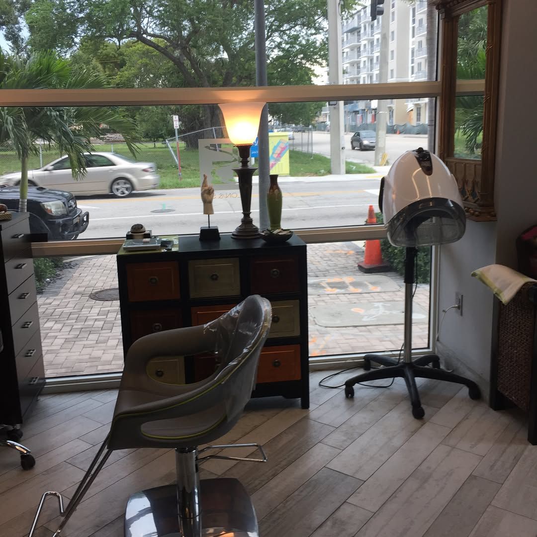 Hair salon interior with chair, dryer, cabinet, lamp, and street view through window.