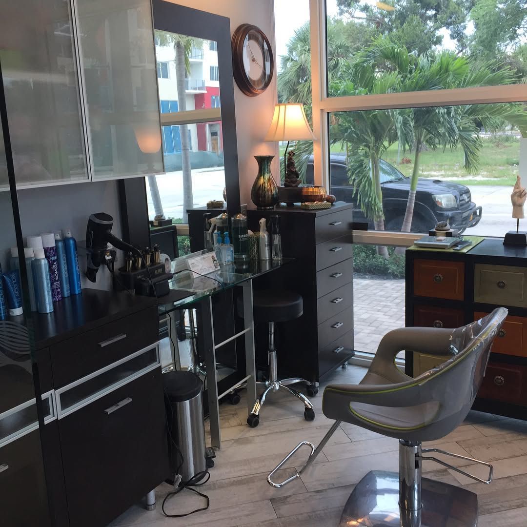Hair salon interior with black cabinetry, styling chair, products, and window with outdoor view.