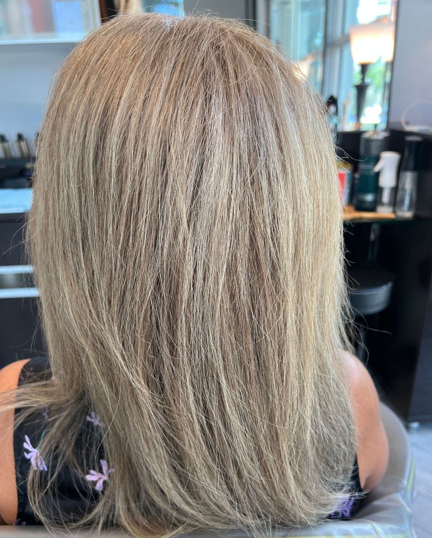 Back view of a person with long, light blonde hair at a salon.