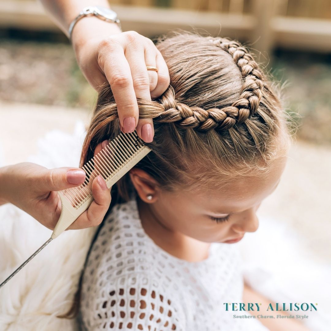 Woman braiding a girl's hair, outdoors. Girl has a crown braid; woman uses a comb.