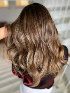 Man in salon with black apron and tattoos stands next to a gray hair chair, inside.