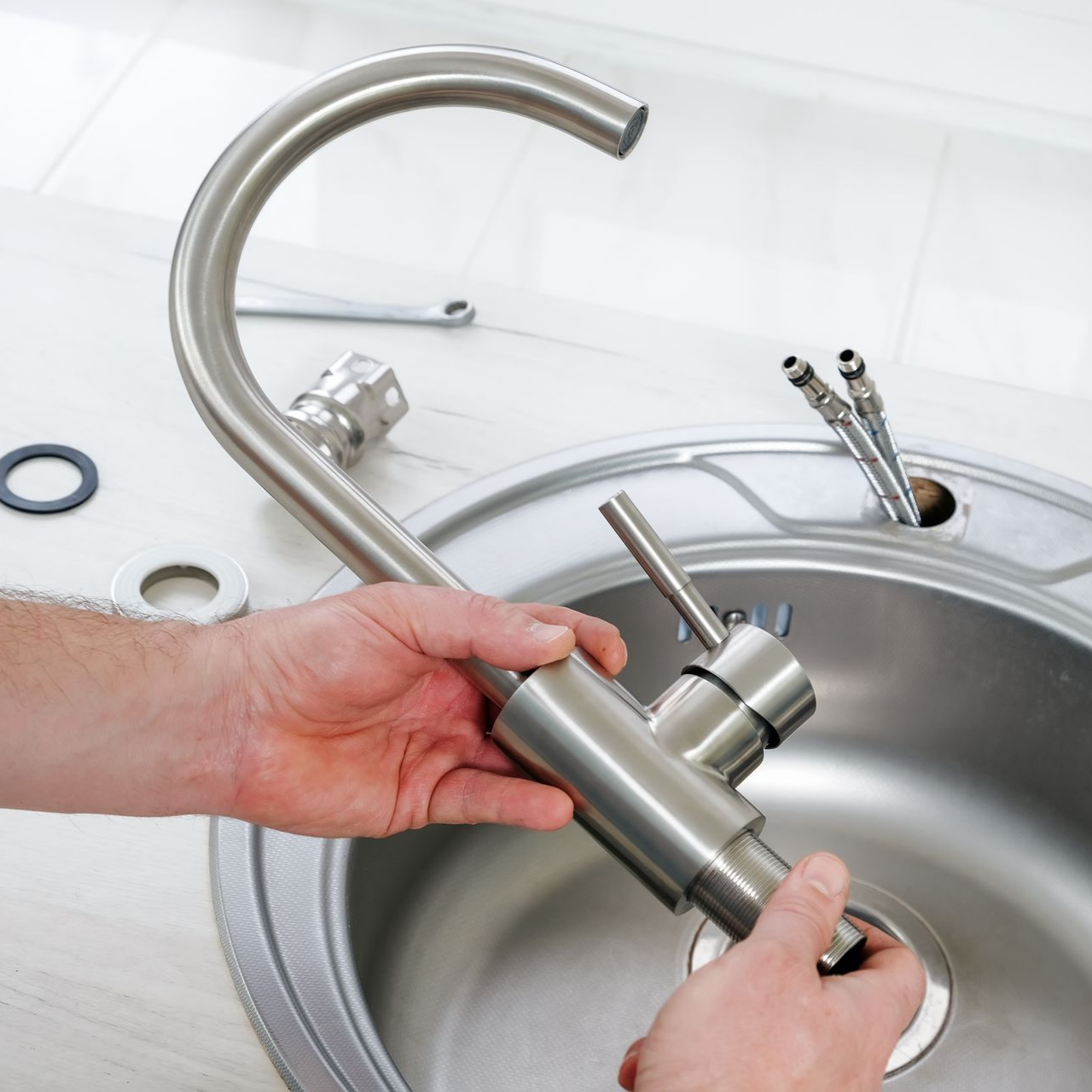 Hands installing a stainless steel kitchen faucet in a sink.