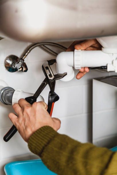Plumber using pliers to work on pipes under a sink.