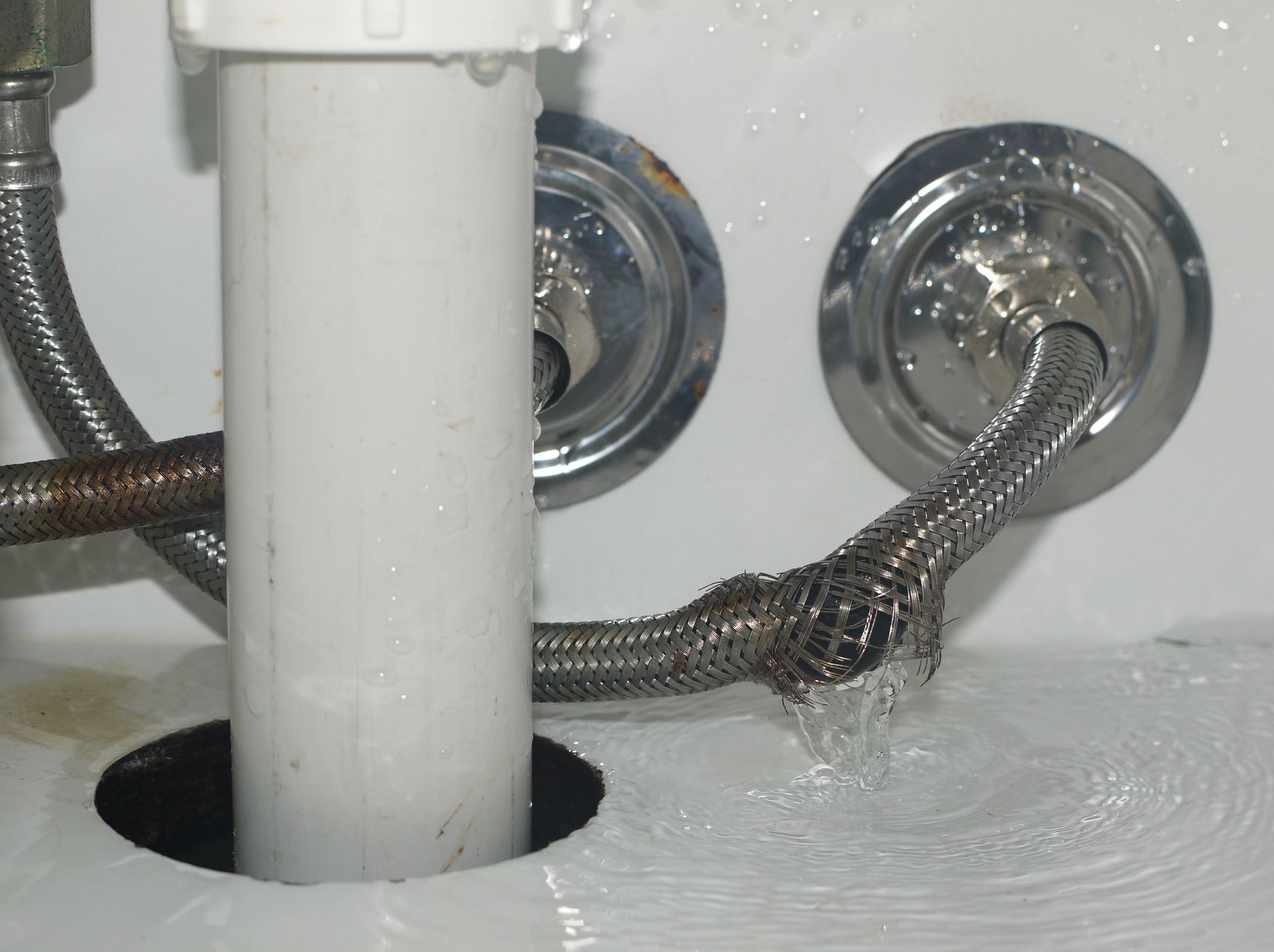 Leaking braided metal supply line under a sink, water spraying out.