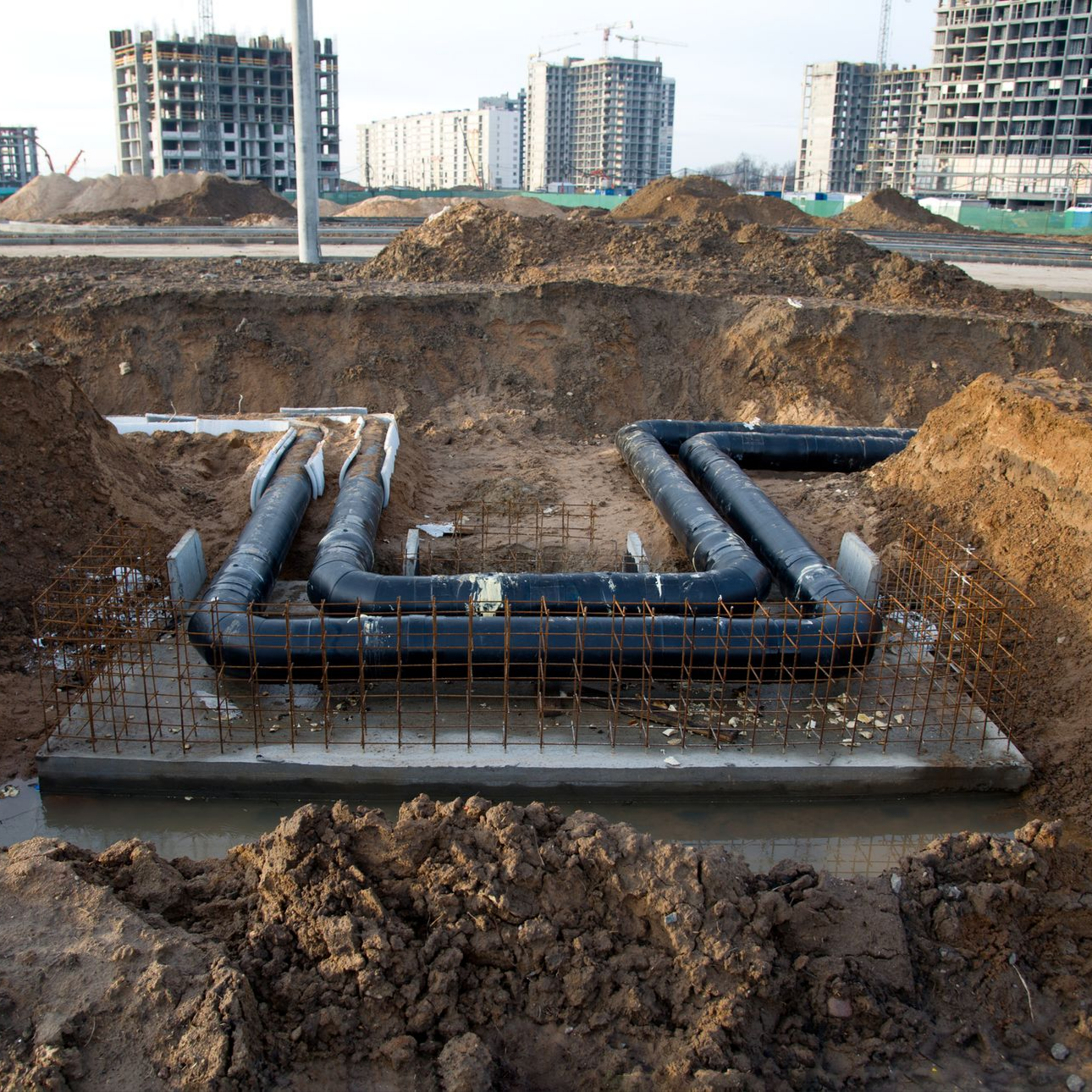 Underground water pipes in a construction site, with dirt mounds and unfinished buildings in the background.