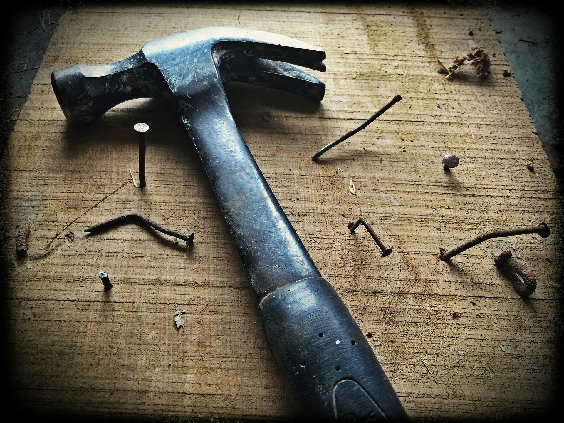 Hammer on a wood surface with partially hammered, bent, and scattered nails.