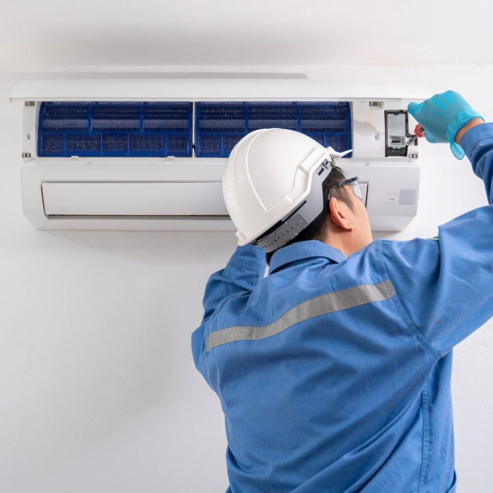 a man wearing a hard hat is working on an air conditioner .