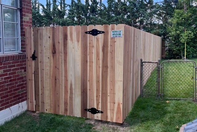 Black metal fence with small gate, green grass, and a building in the background.