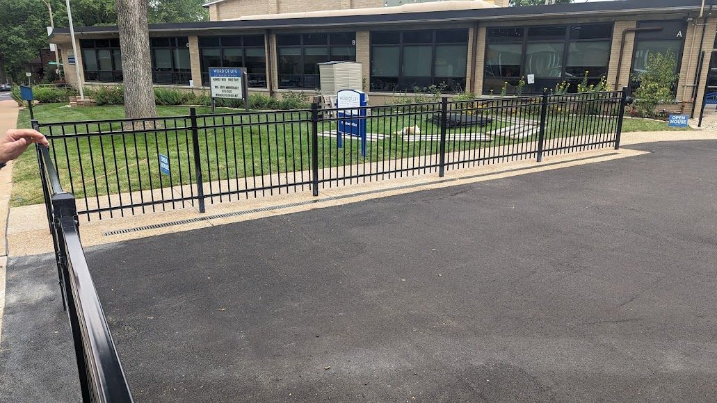 Black metal fence with small gate, green grass, and a building in the background.