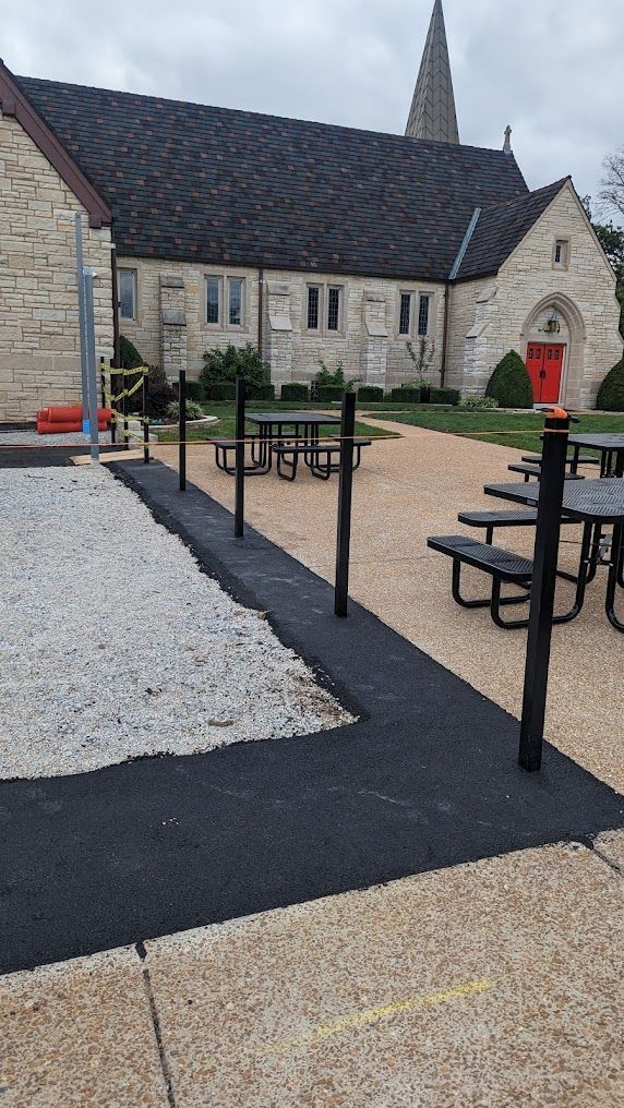 Outdoor patio with picnic tables near a church. Paved paths, gravel and black railing are visible.
