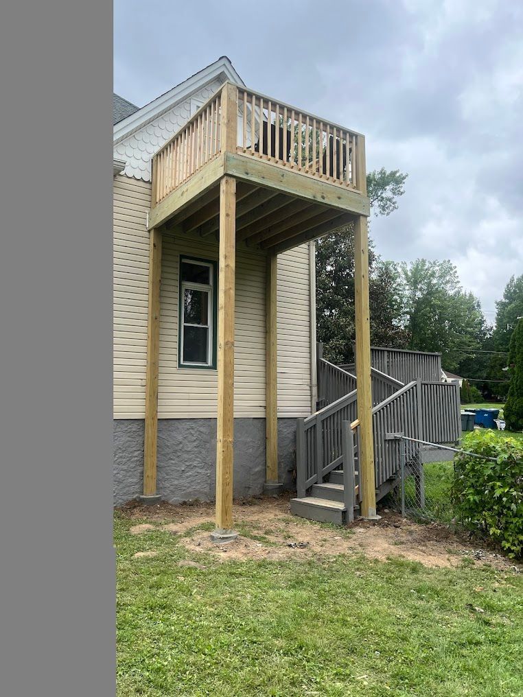 Elevated wooden deck attached to a house, supported by posts. Includes stairs and a railing.