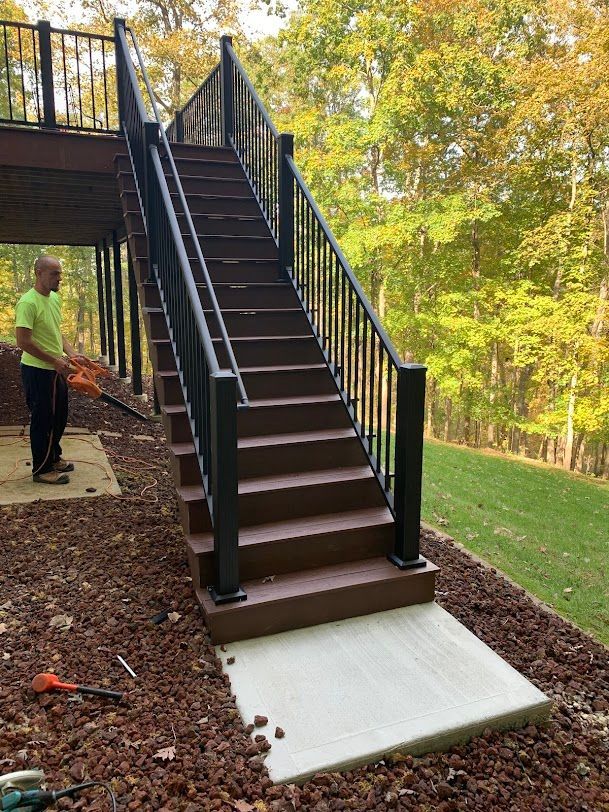 Wooden staircase with black railings leads up a hill; a person works nearby.