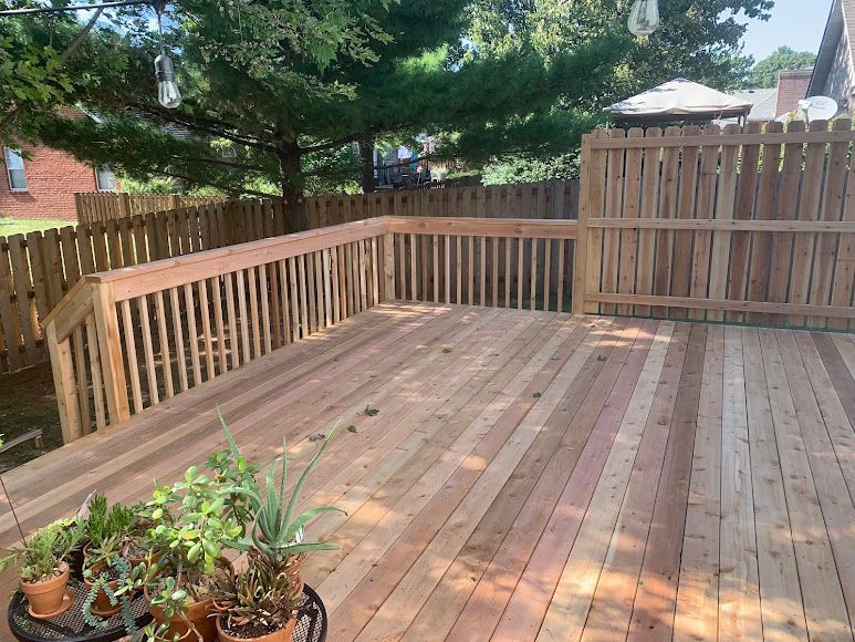 Wooden deck with railing and plants, bordered by a wooden fence.