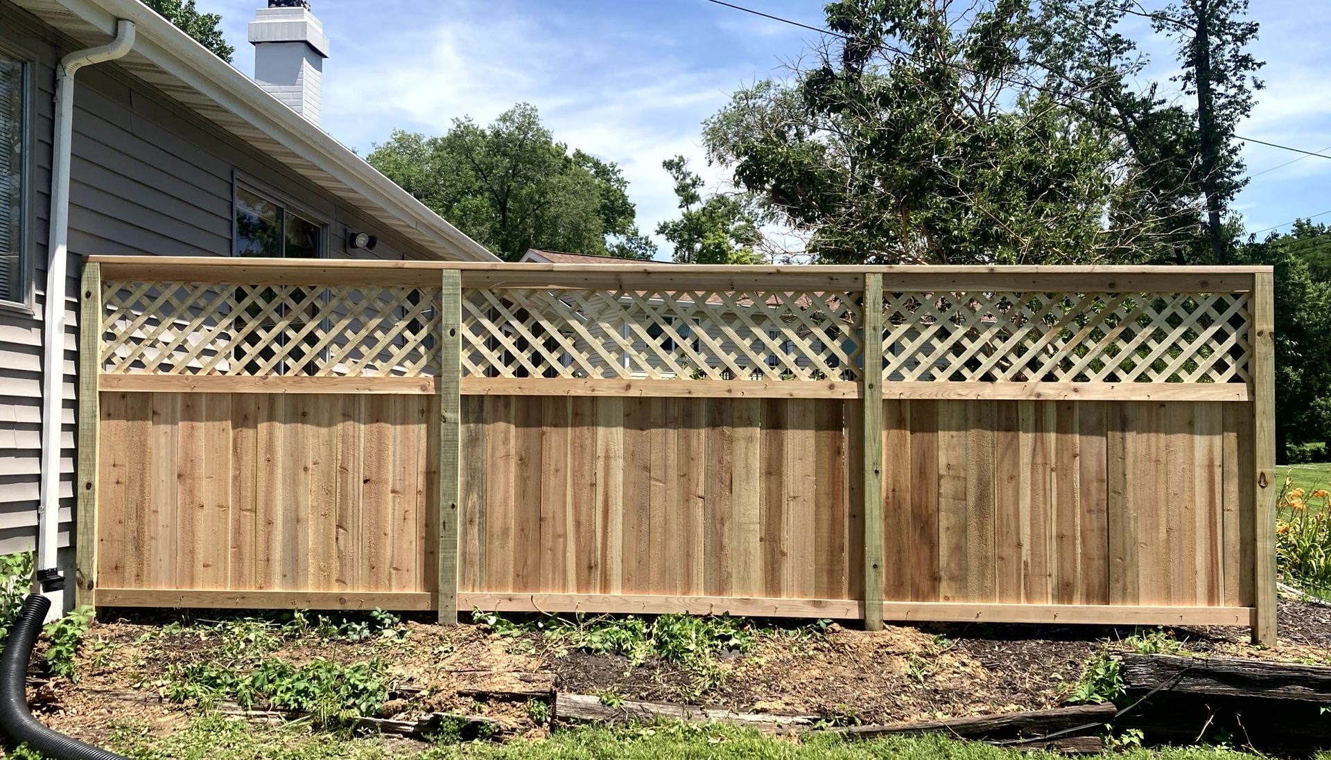 Black metal fence with small gate, green grass, and a building in the background.