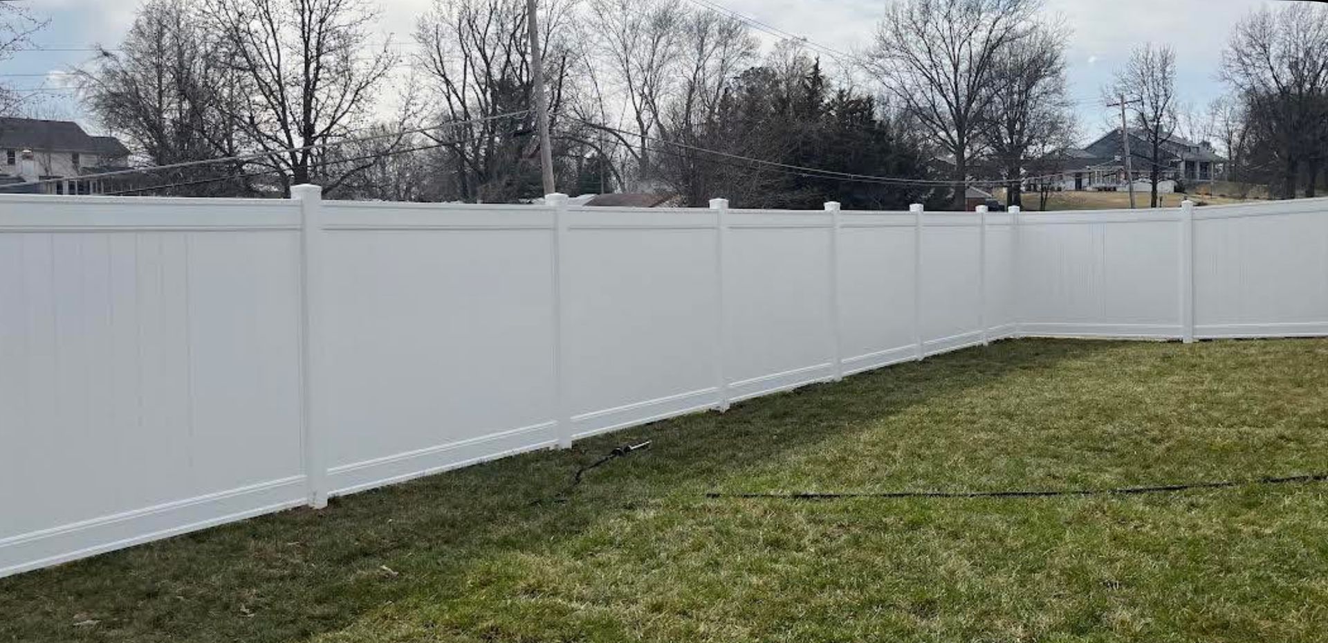 Black metal fence with small gate, green grass, and a building in the background.