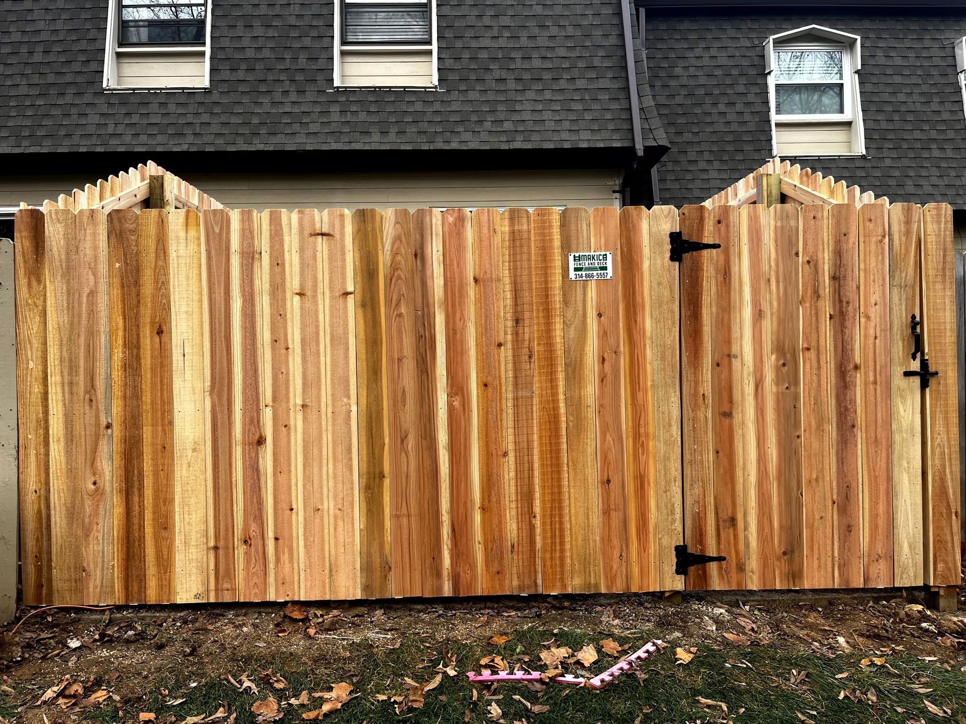 Black metal fence with small gate, green grass, and a building in the background.