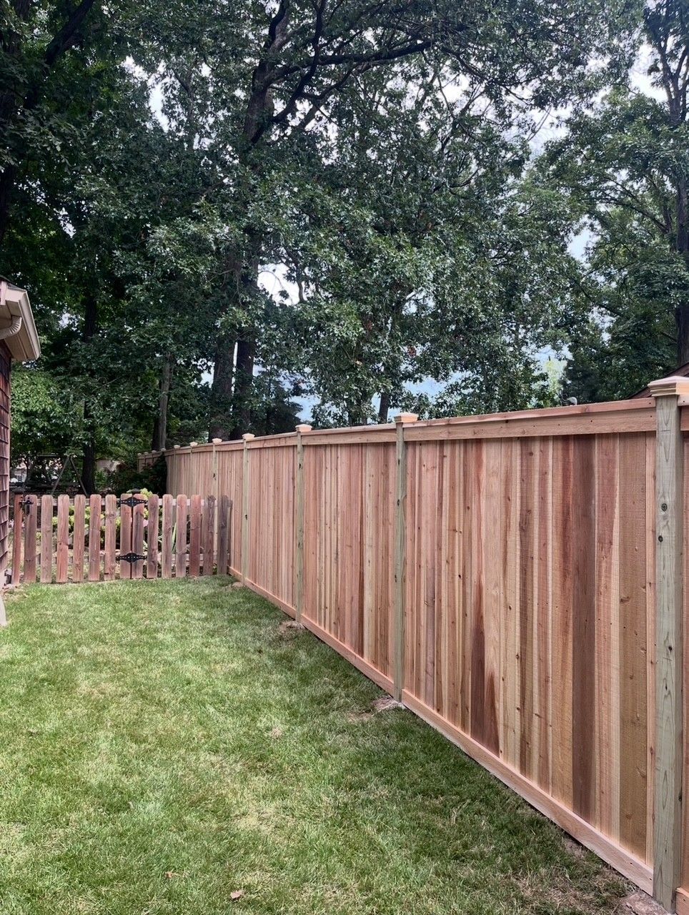 Black metal fence with small gate, green grass, and a building in the background.
