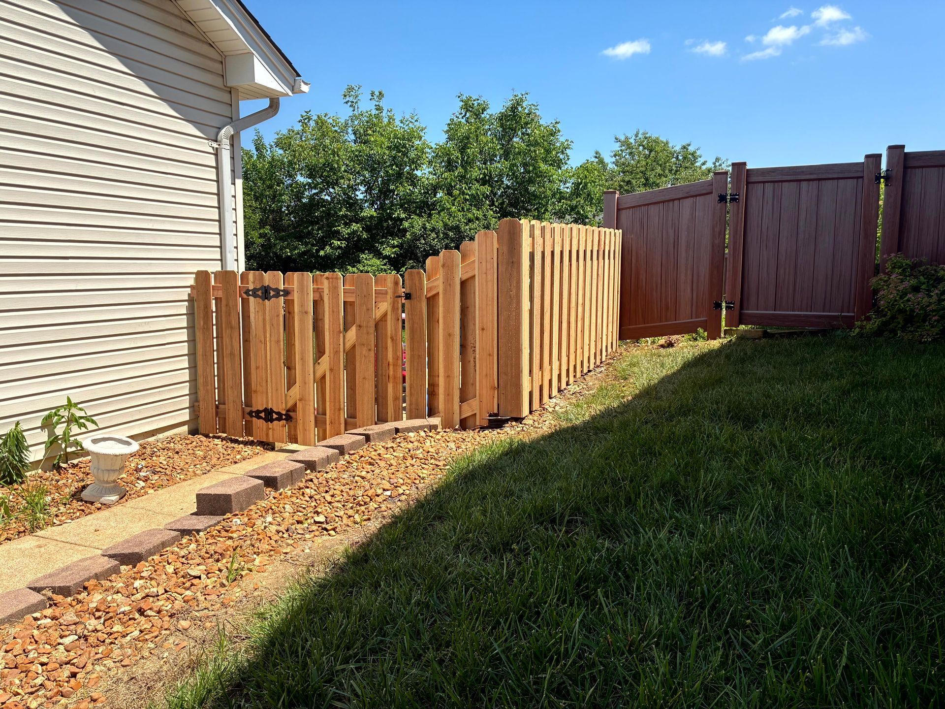 Black metal fence with small gate, green grass, and a building in the background.