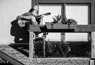 A man is sitting on a balcony playing a guitar.