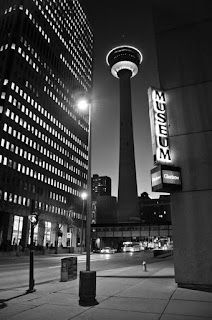 A black and white photo of a city street at night featuring the Calgary tower.