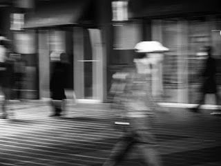 A blurry black and white photo of people walking down a street.