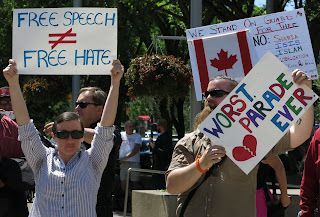 Anti-Islam Protesters and Counter-protesters at City Hall Calgary. A woman is holding a sign that says free speech does not equal free hate. A man holds one that says worst parade ever