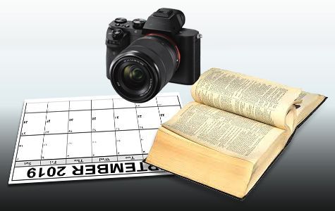 A camera is sitting on top of a calendar next to an open book, possibly a dictionary.