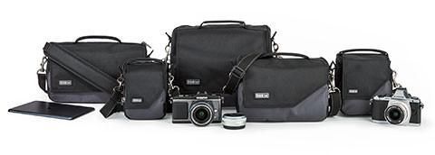 several camera bags, cameras, lenses and a laptop arranged on a table