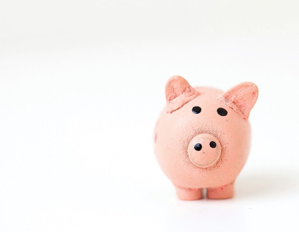 A pink piggy bank with black eyes is standing on a white surface.