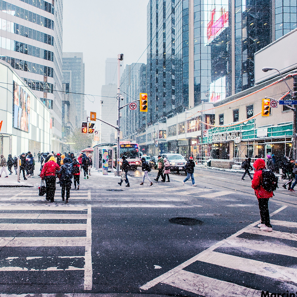 A group of people are crossing a city street in the snow