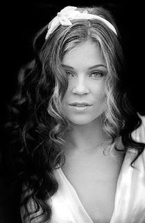 A black and white photo of a woman with long curly hair wearing a headband.
